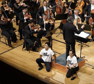Die beiden Aktivisten kleben sich am Dirigentenpult fest, während das Orchester weiterspielt