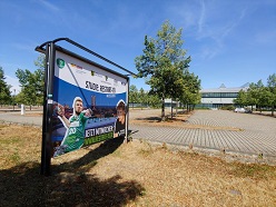 Vor der Arena Leipzig weist ein Schild auf das Experiment im Rahmen des Projektes RESTART-19 hin  Universitätsmedizin Halle (Saale)